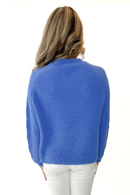Back view of woman wearing Blue Ribbed Sweater with jeans against white studio background.