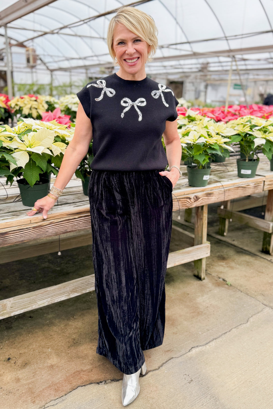 Woman in a black outfit with silver bow details standing by holiday decor.