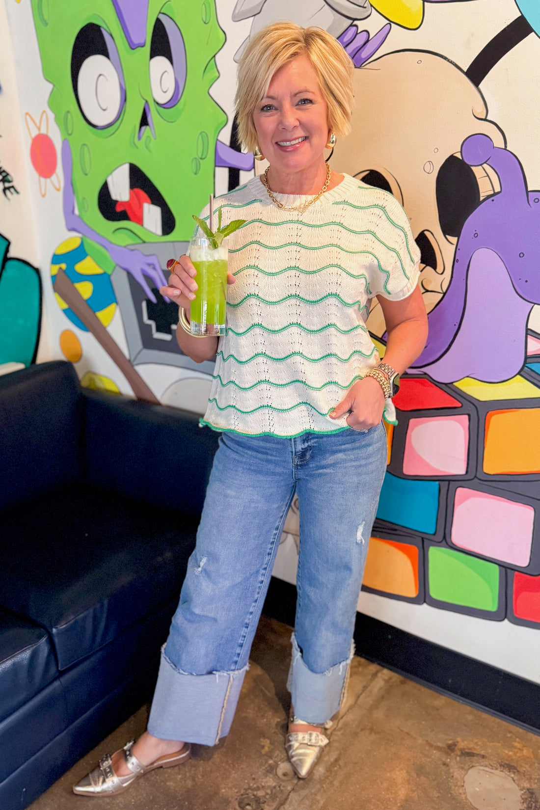 Front view of woman wearing Green &amp; Cream Scallop Detail Short Sleeve Sweater with jeans at a bar.