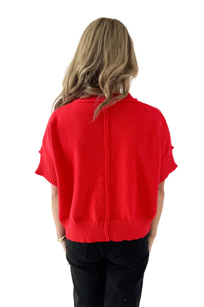 Back view of woman wearing red half sleeve sweater with jeans against white studio background.