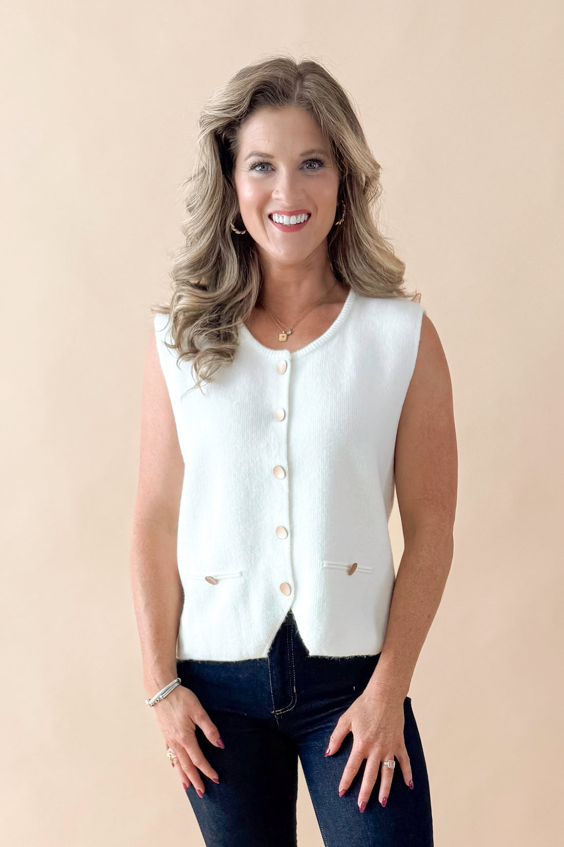 Front view of woman wearing Cream Button Detail Sweater Vest with jeans against tan studio background.