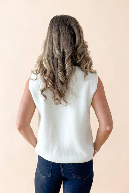 Back view of woman wearing Cream Button Detail Sweater Vest with jeans against tan studio background.