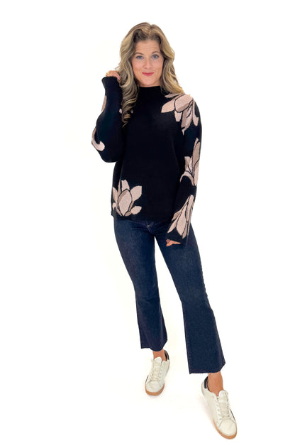 Front view of woman wearing Black With Mauve Floral Print Sweater with jeans against white studio background.