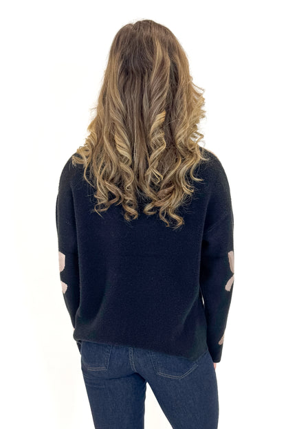 Back view of woman wearing Black With Mauve Floral Print Sweater with jeans against white studio background.