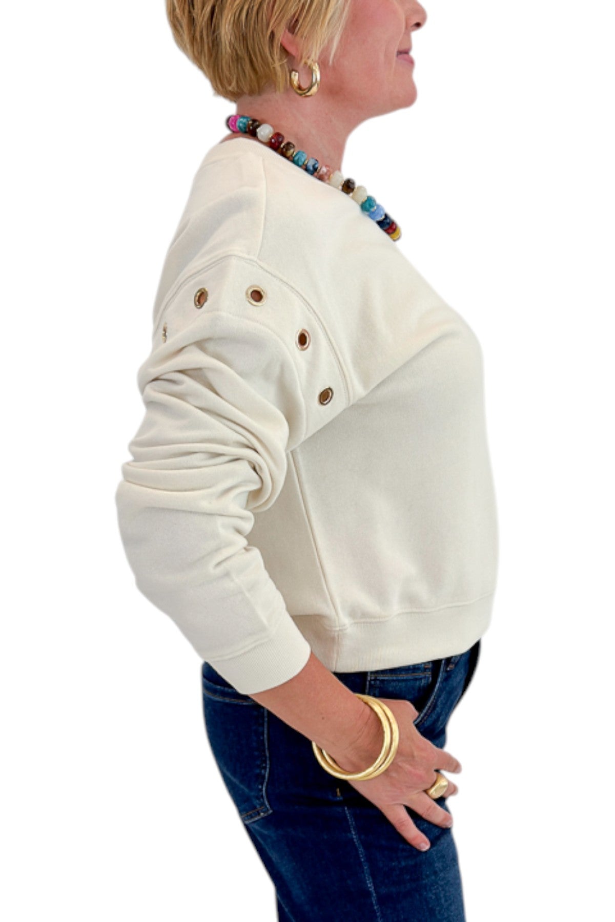 Side detail view of woman wearing Swagger Boutique’s Sandstone Axel Grommet Sweatshirt by Z Supply with jeans against white studio background.