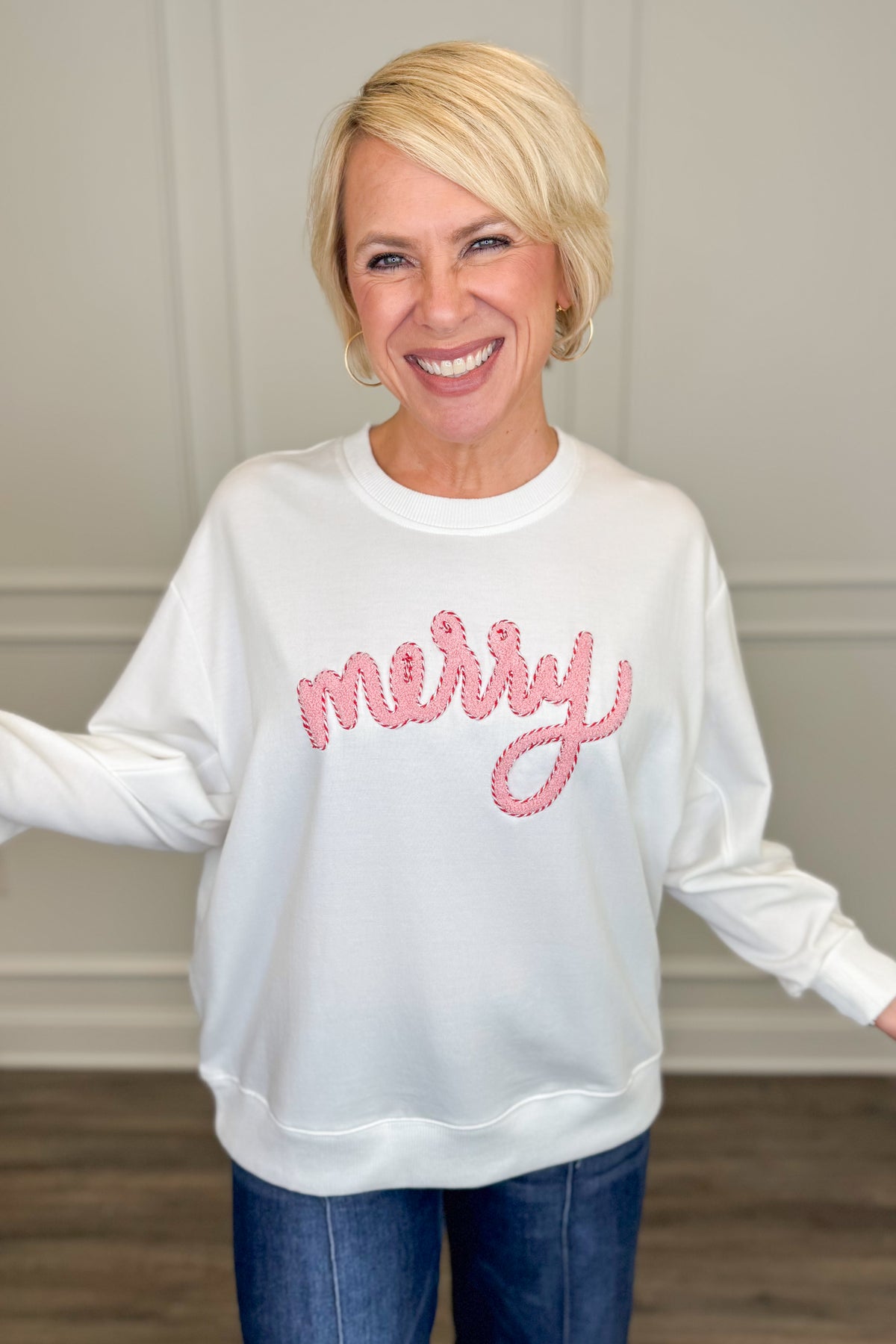 A smiling blonde woman wearing a white crewneck sweatshirt with &