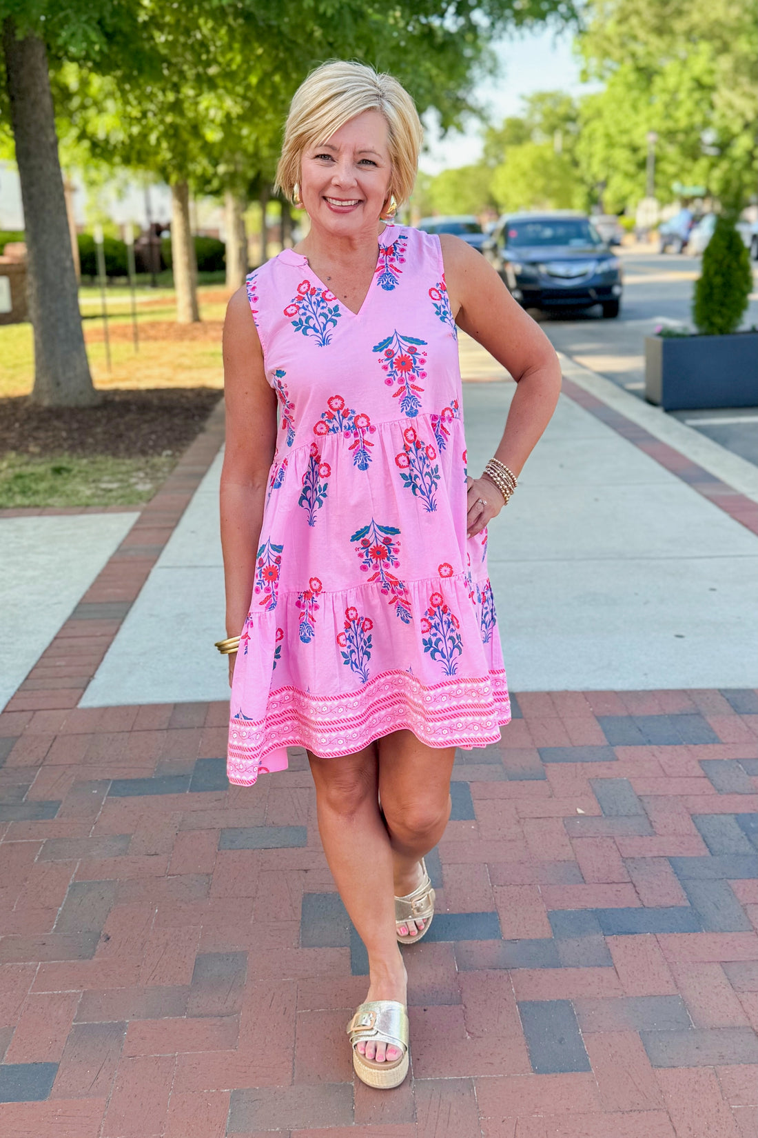 Front view of woman wearing Pink Printed Sarajane Sleeveless Dress by MudPie walking outside.