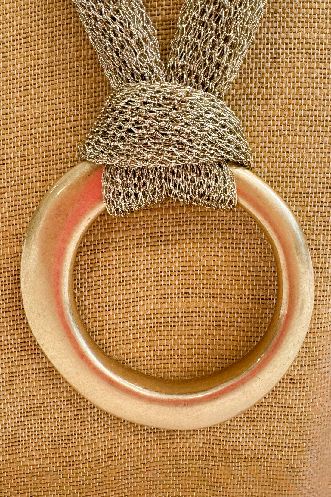 Gold ring with textured mesh chain on a beige fabric background
