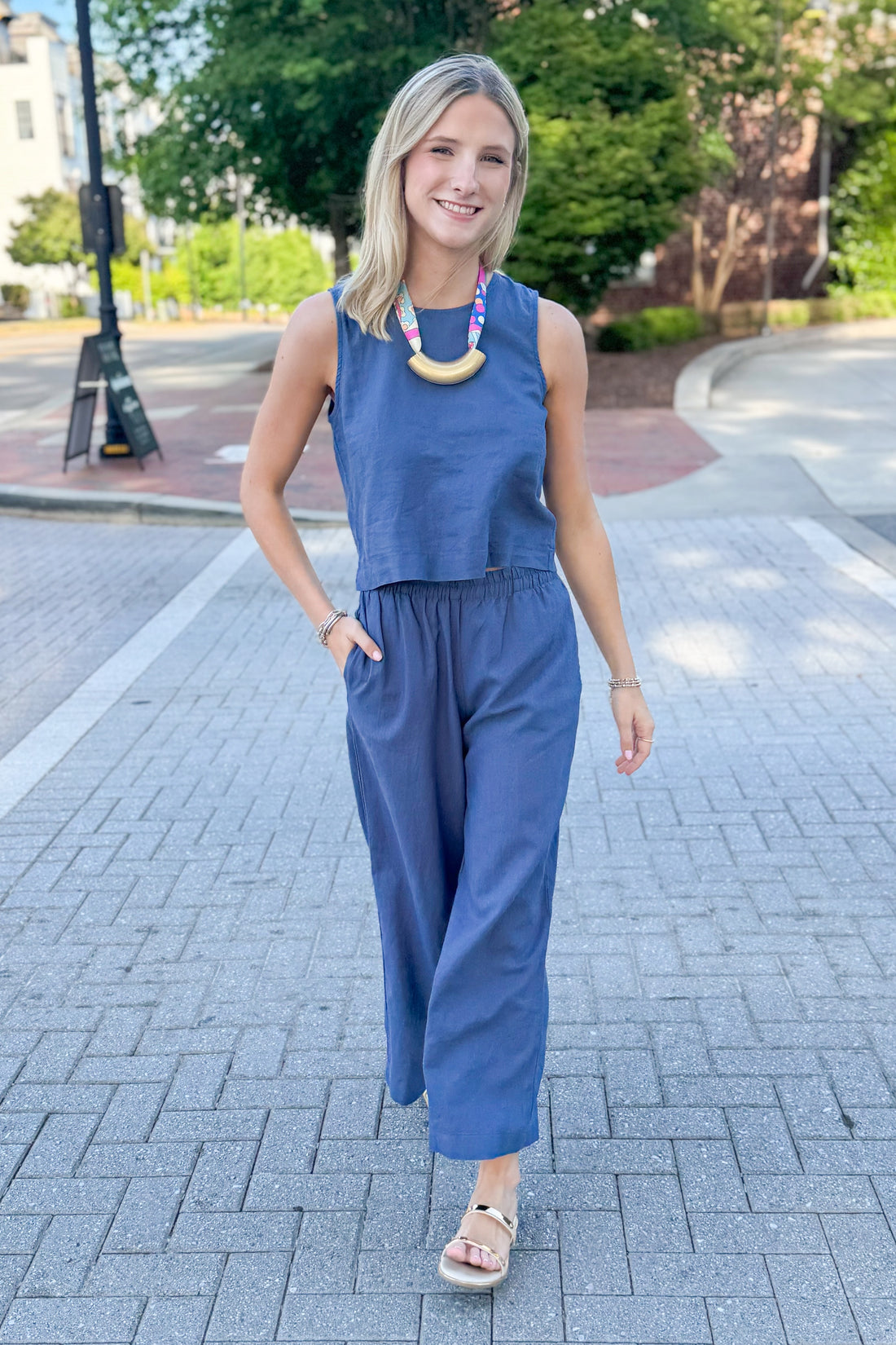 Front view of woman wearing Vintage Indigo Scout Linen Pants by Z Supply with matching Vintage Indigo Sloane Linen Top by Z Supply walking outside.