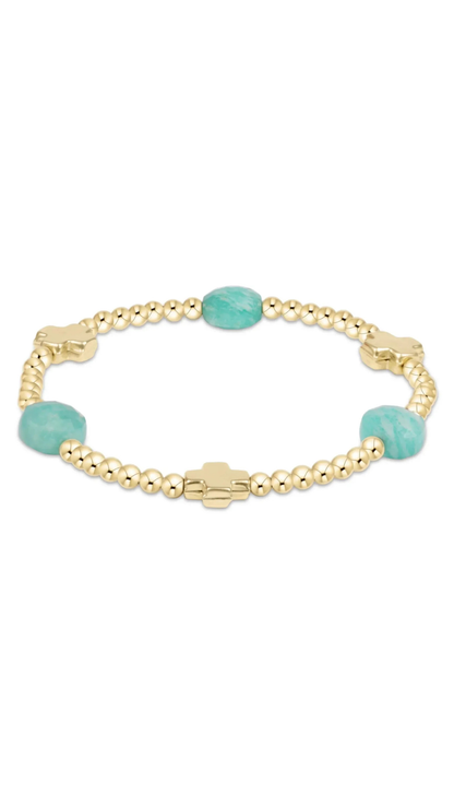 A gold beaded bracelet featuring two oval light blue-green turquoise beads and a gold cross clasp, displayed on a clean white background.