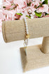 Pearl bracelet on a burlap stand with pink flowers in the background