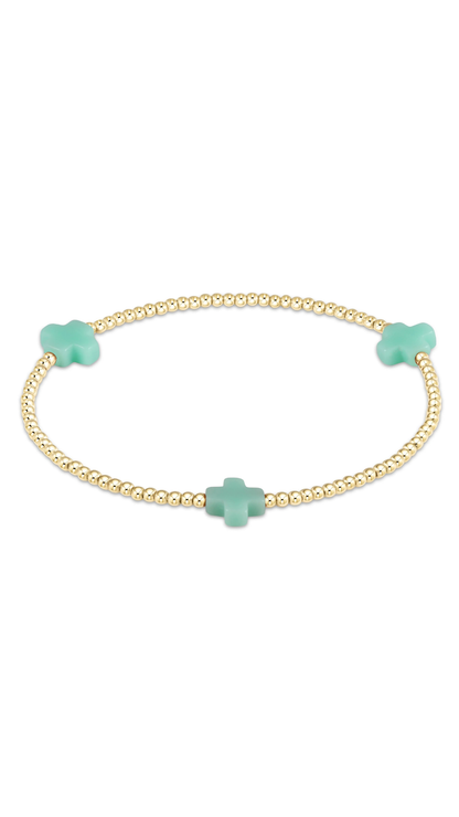 A delicate gold beaded bracelet featuring three mint green charms, including two small clover-shaped charms and one larger cross-shaped charm, displayed on a clean white background.
