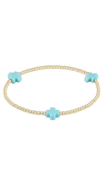 A delicate gold beaded bracelet featuring three turquoise cross charms, displayed on a clean white background.