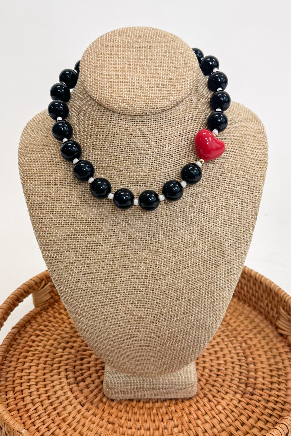 Black beaded necklace with a red heart pendant on a beige bust