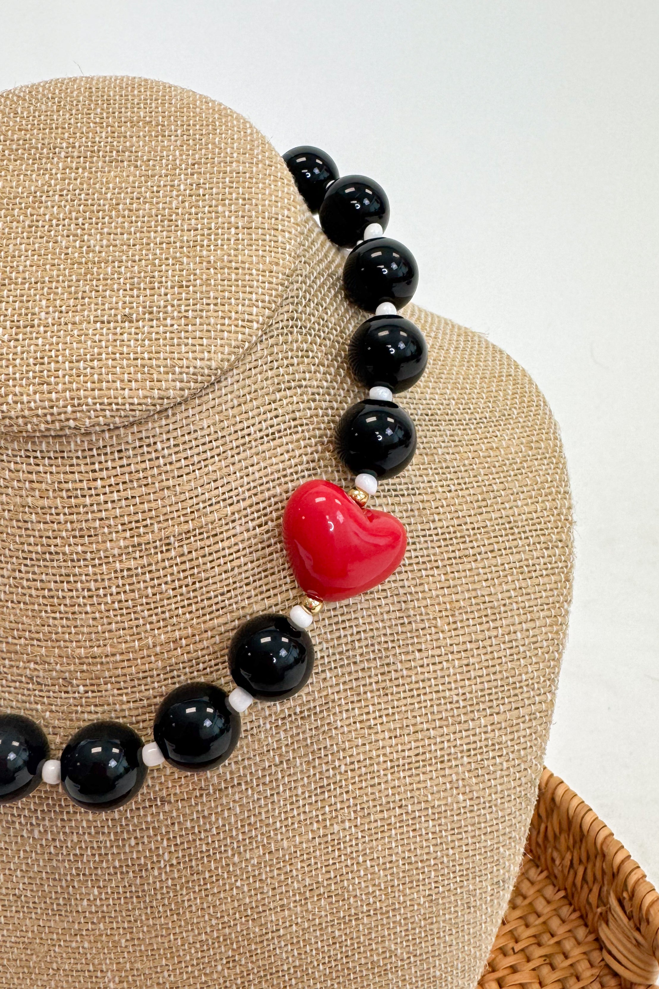 Necklace with black beads and a red heart-shaped charm on a mannequin bust.