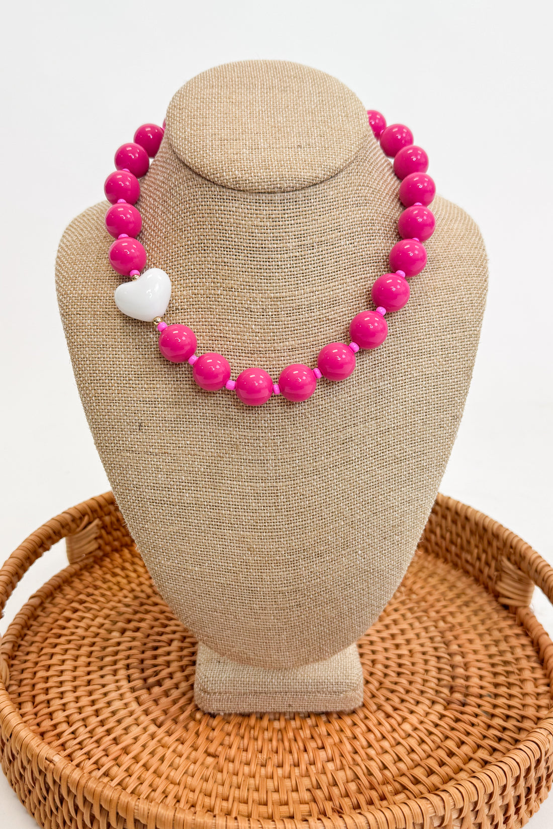 Necklace with pink beads and a white heart on a beige bust
