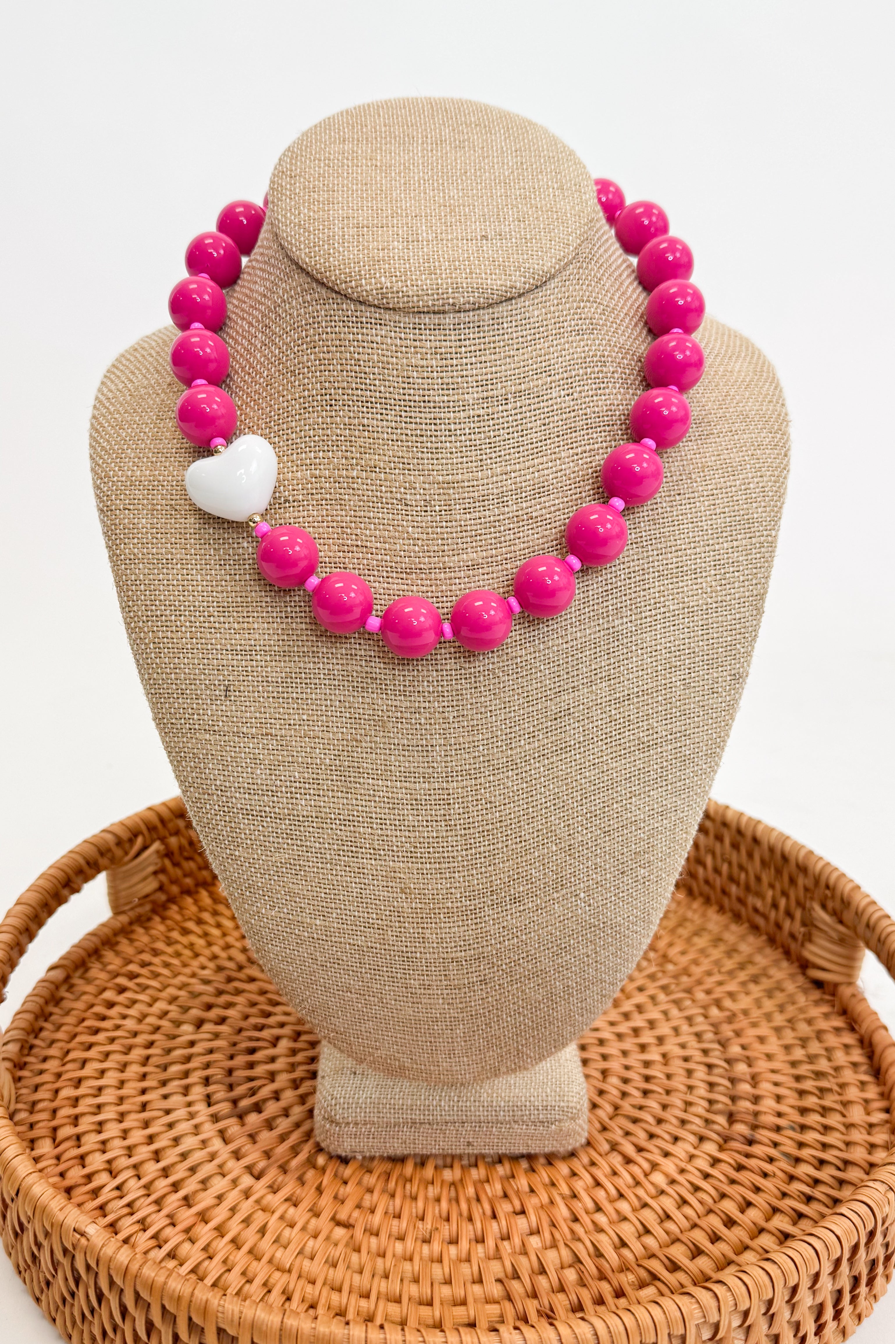 Necklace with pink beads and a white heart on a beige bust
