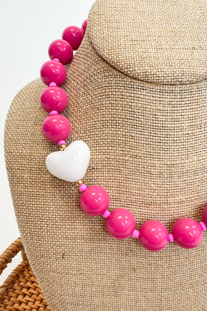 Necklace with pink beads and a white heart pendant on a beige mannequin.