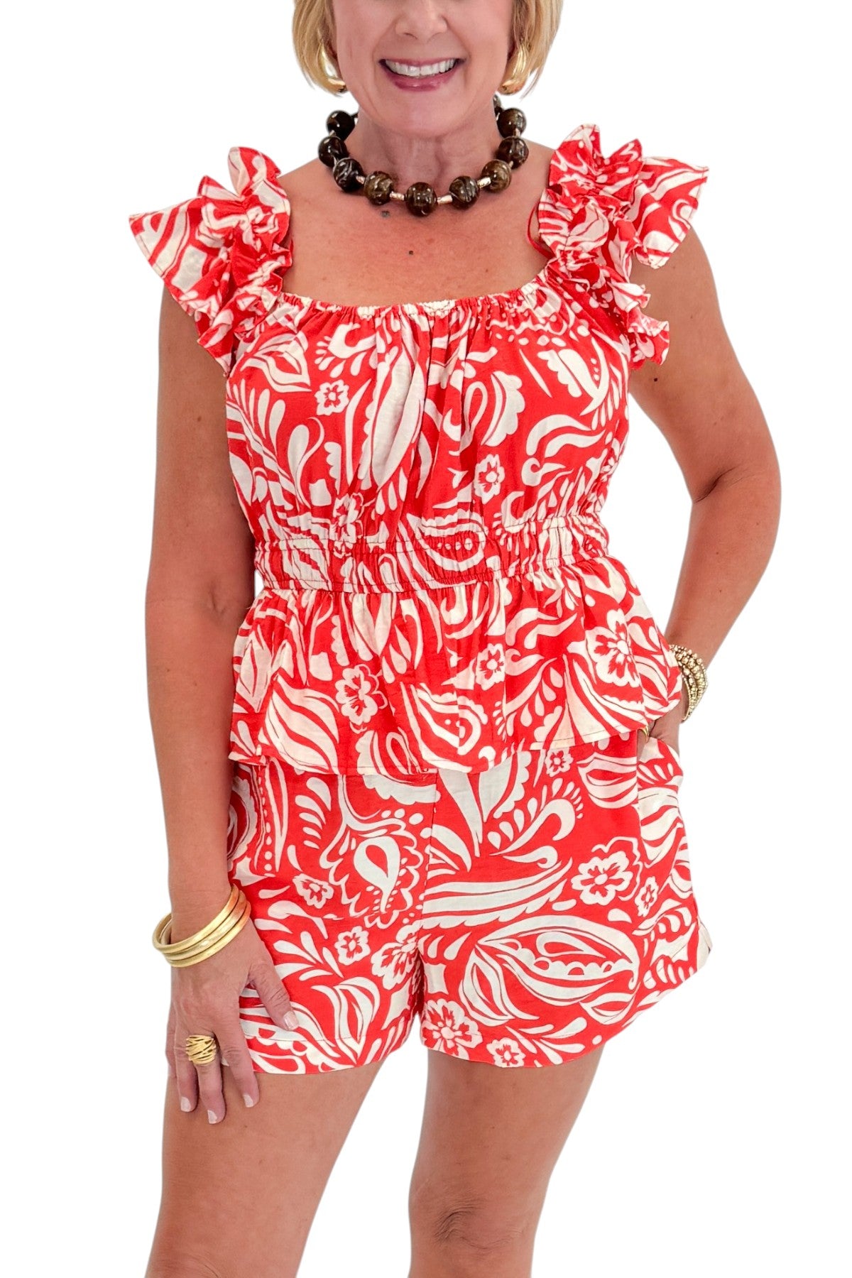 Front detail view of woman wearing Swagger Boutique’s Coral Printed Smocked Peplum Tank with matching Coral Printed Shorts against white studio background.