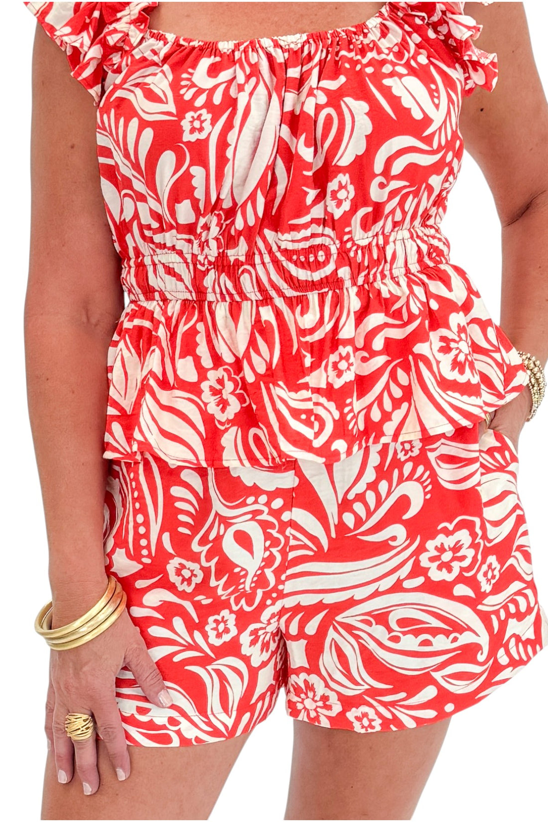 Front detail view of woman wearing Swagger Boutique’s Coral Printed Smocked Peplum Tank with matching Coral Printed Shorts against white studio background.