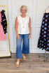 Front view of woman wearing Swagger Boutique’s Smocked Edge Detail Casual Tank Top with jeans with clothing hanging in the background.