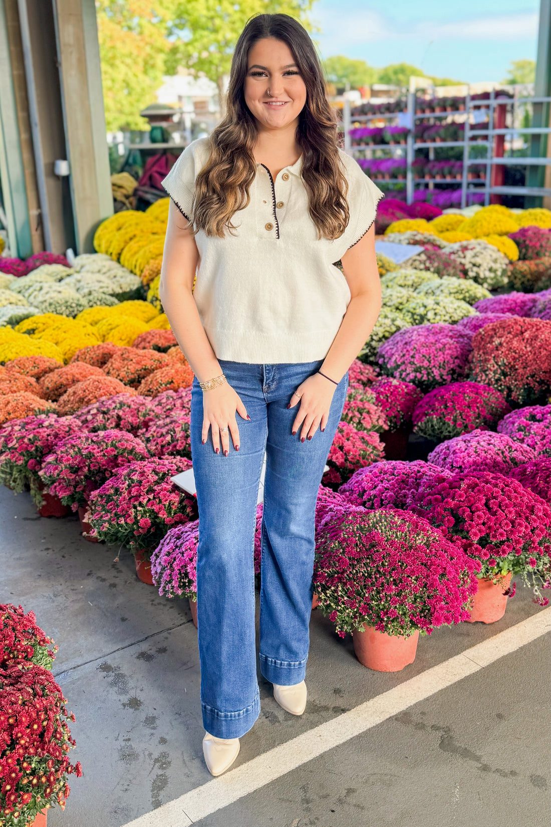 Outdoor picture of woman wearing Cream With Black Stitching Short Sleeve Sweater by Entro and jeans with mums in the background.