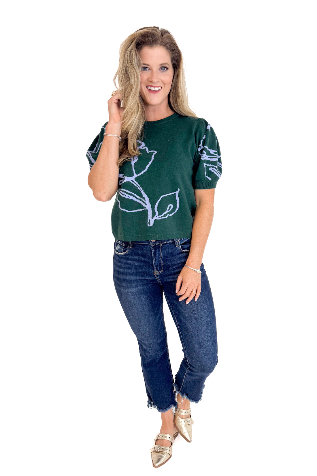 Woman wearing a dark green t-shirt with a floral design and blue jeans on a white background