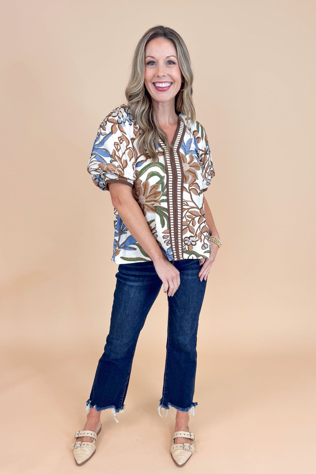 Woman wearing a patterned blouse and jeans on a beige background