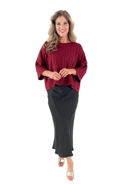 Front view of woman wearing Burgundy Cable Knit 3/4 Sleeve Sweater with black skirt against white studio background.