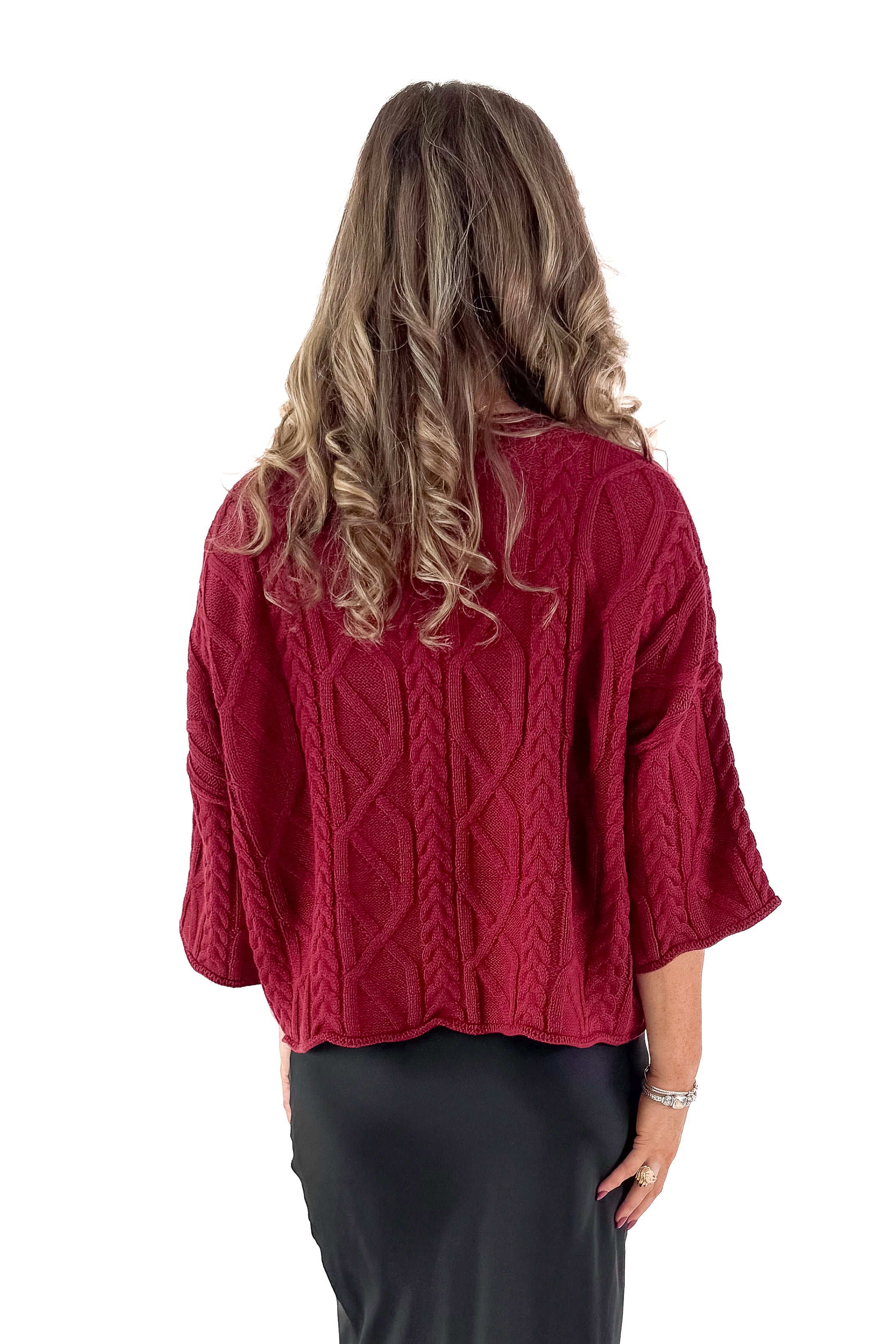 Back view of woman wearing Burgundy Cable Knit 3/4 Sleeve Sweater with black skirt against white studio background.