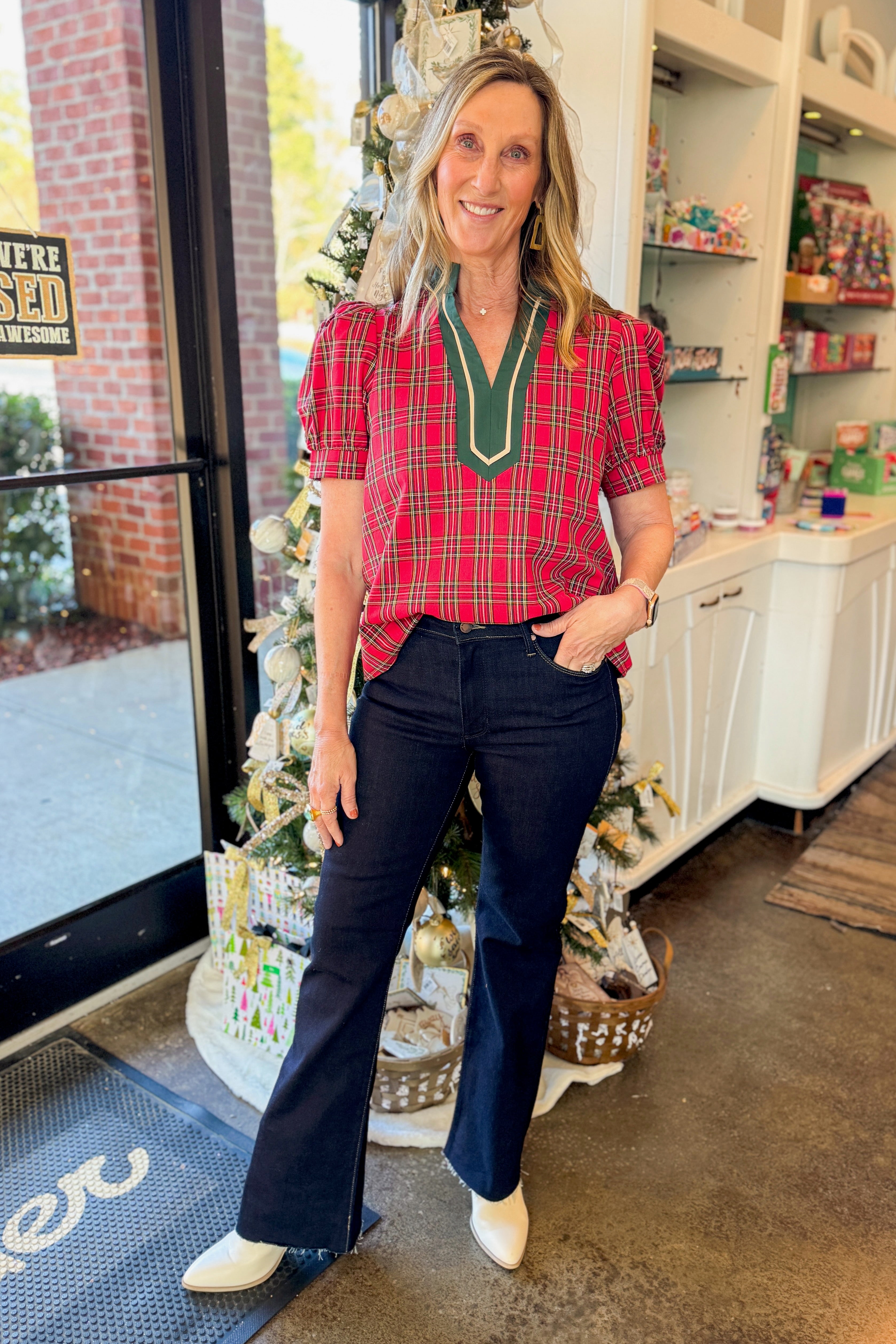 Front view of woman wearing Red Tartan With Green V-neck Detail Top with jeans in a boutique.