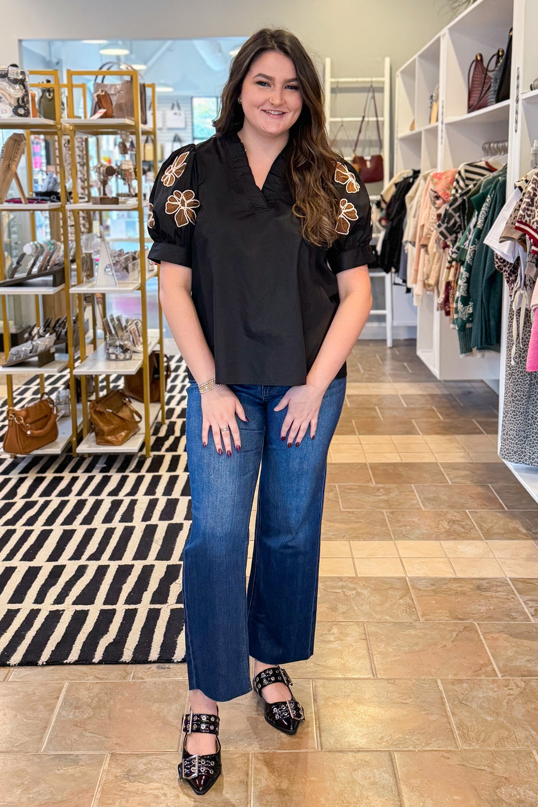 Woman in a black top with floral embellishments and blue jeans standing in a store.
