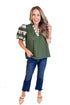 Woman wearing an olive green top with floral details and blue jeans on a white background