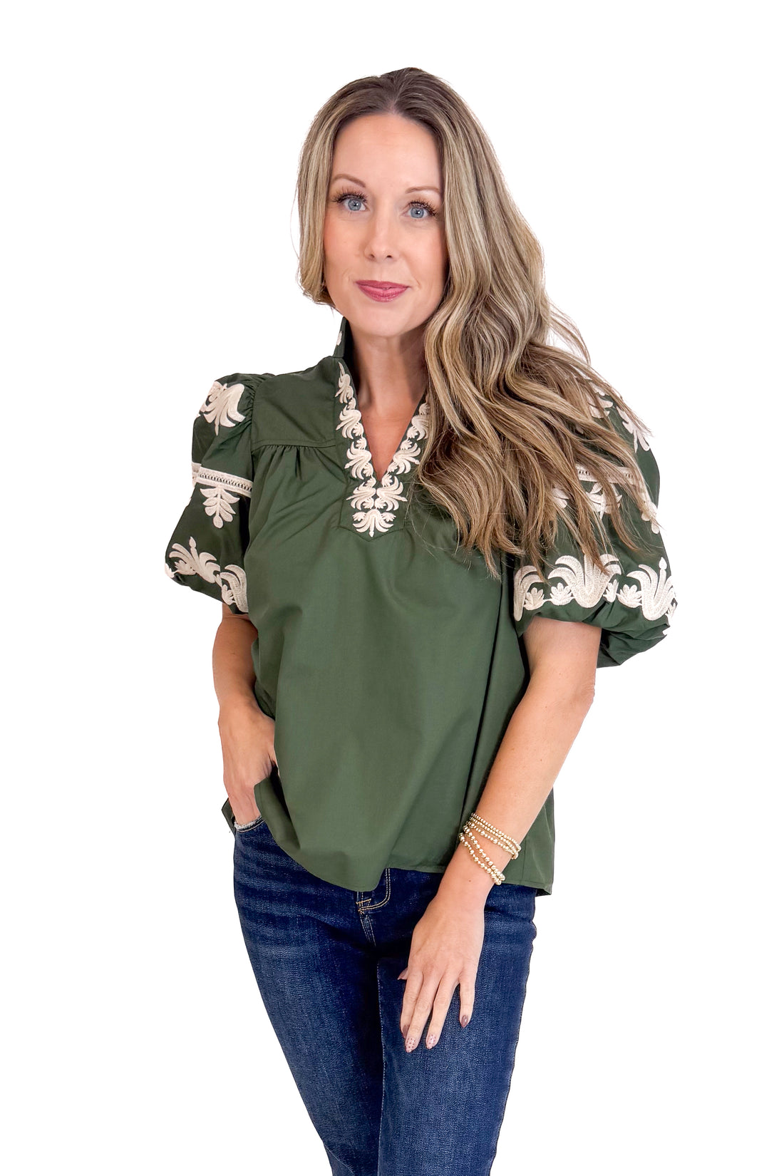 Woman wearing an olive green blouse with floral embroidery on a white background