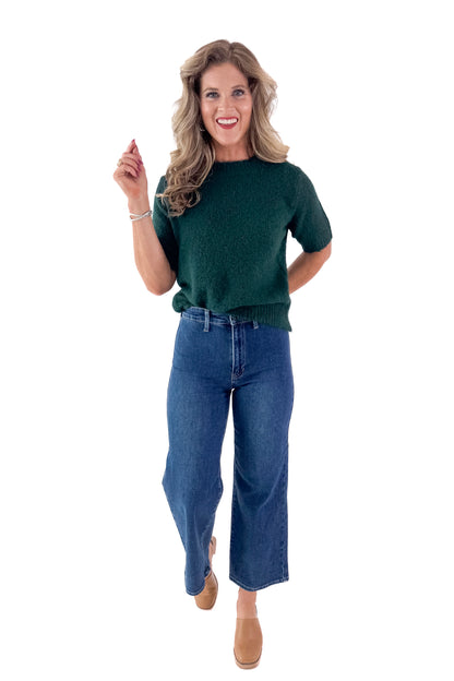 Front view of woman wearing green sweater with jeans and white studio background.