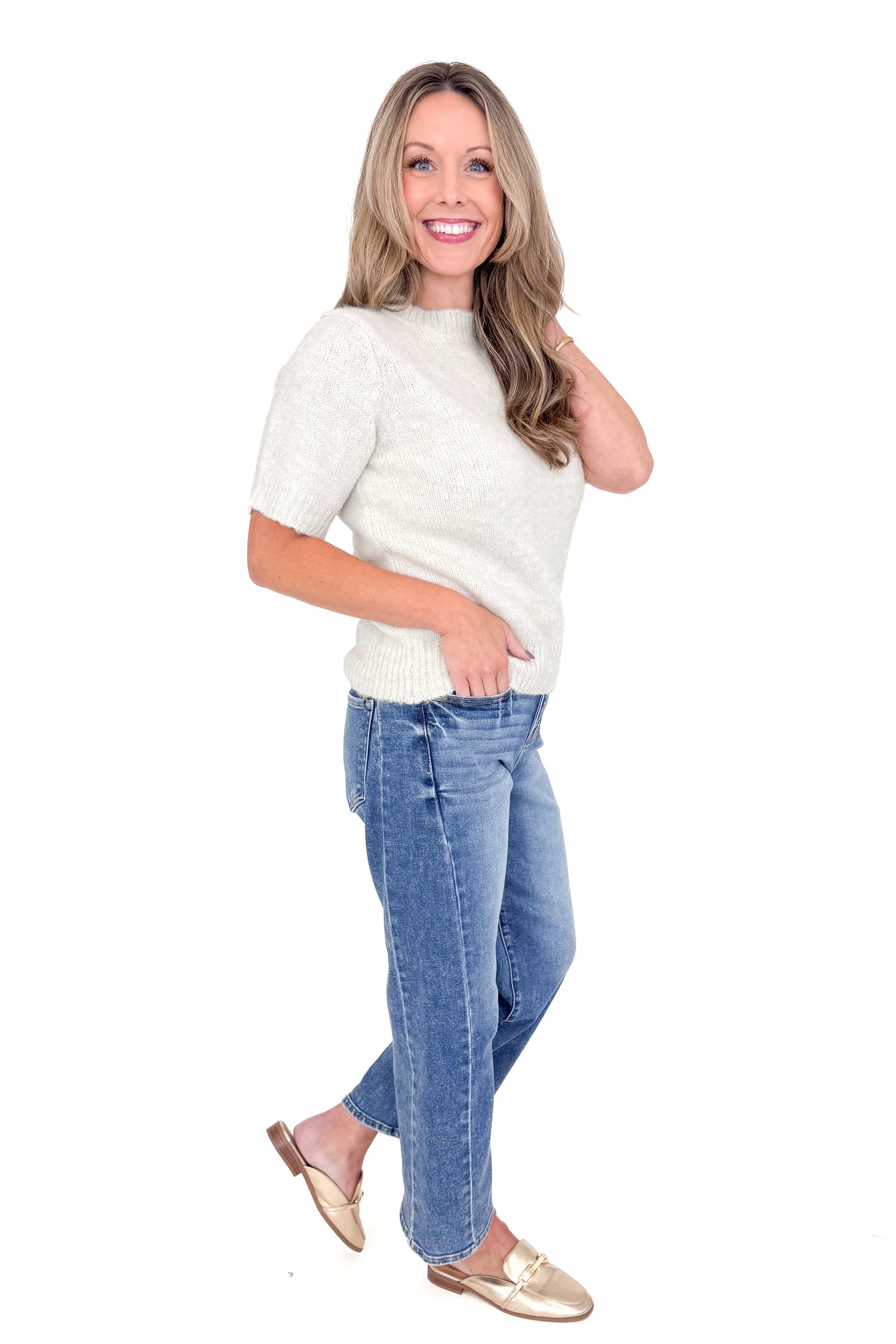 Side view of woman wearing oatmeal color sweater with jeans against white studio background.