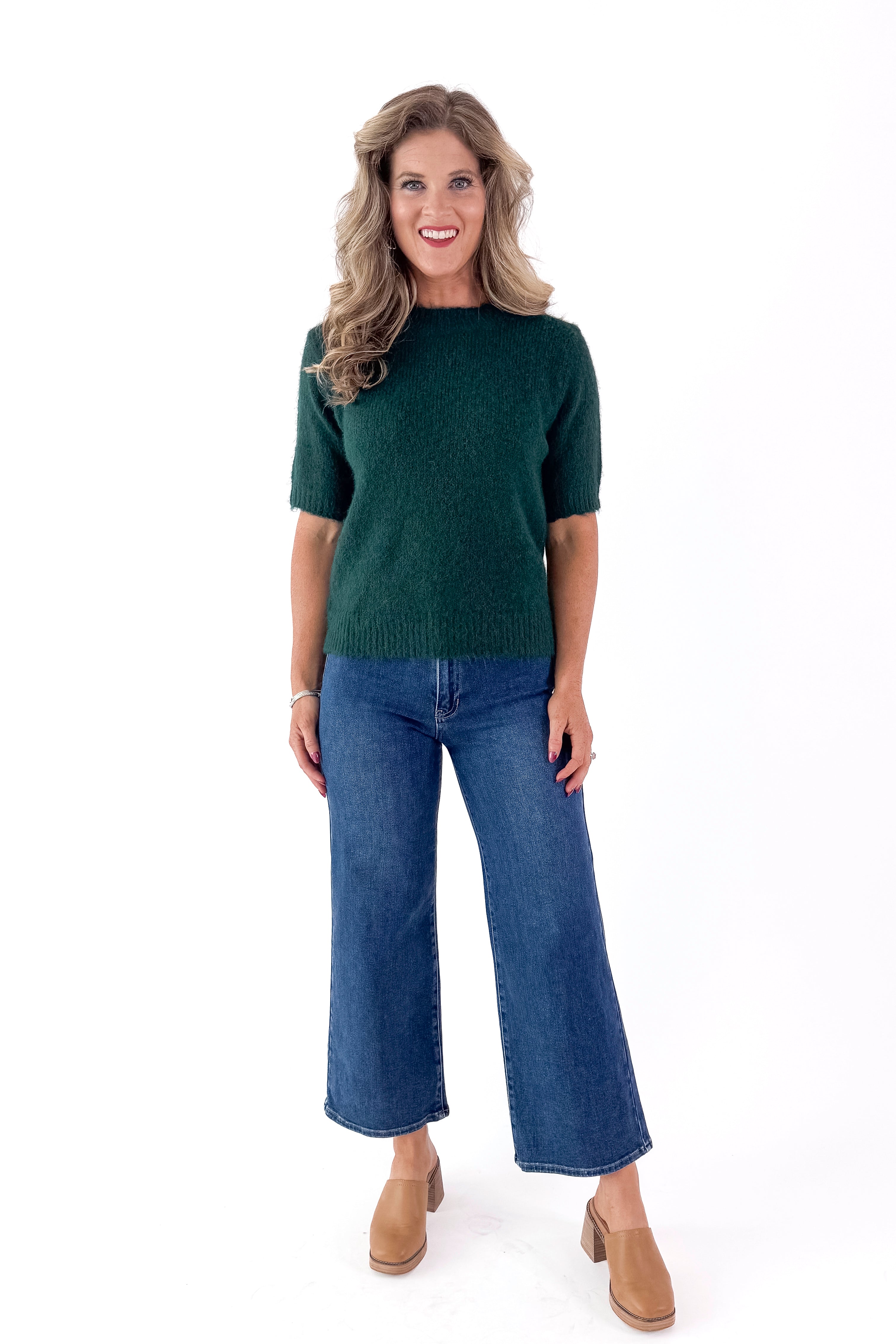 Front view of woman wearing green sweater with jeans and white studio background.