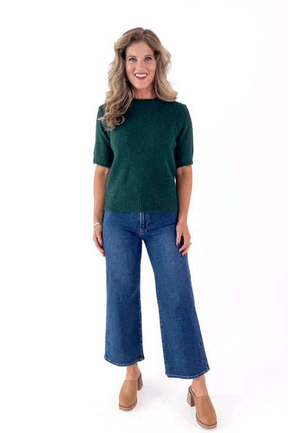 Front view of woman wearing green sweater with jeans and white studio background.
