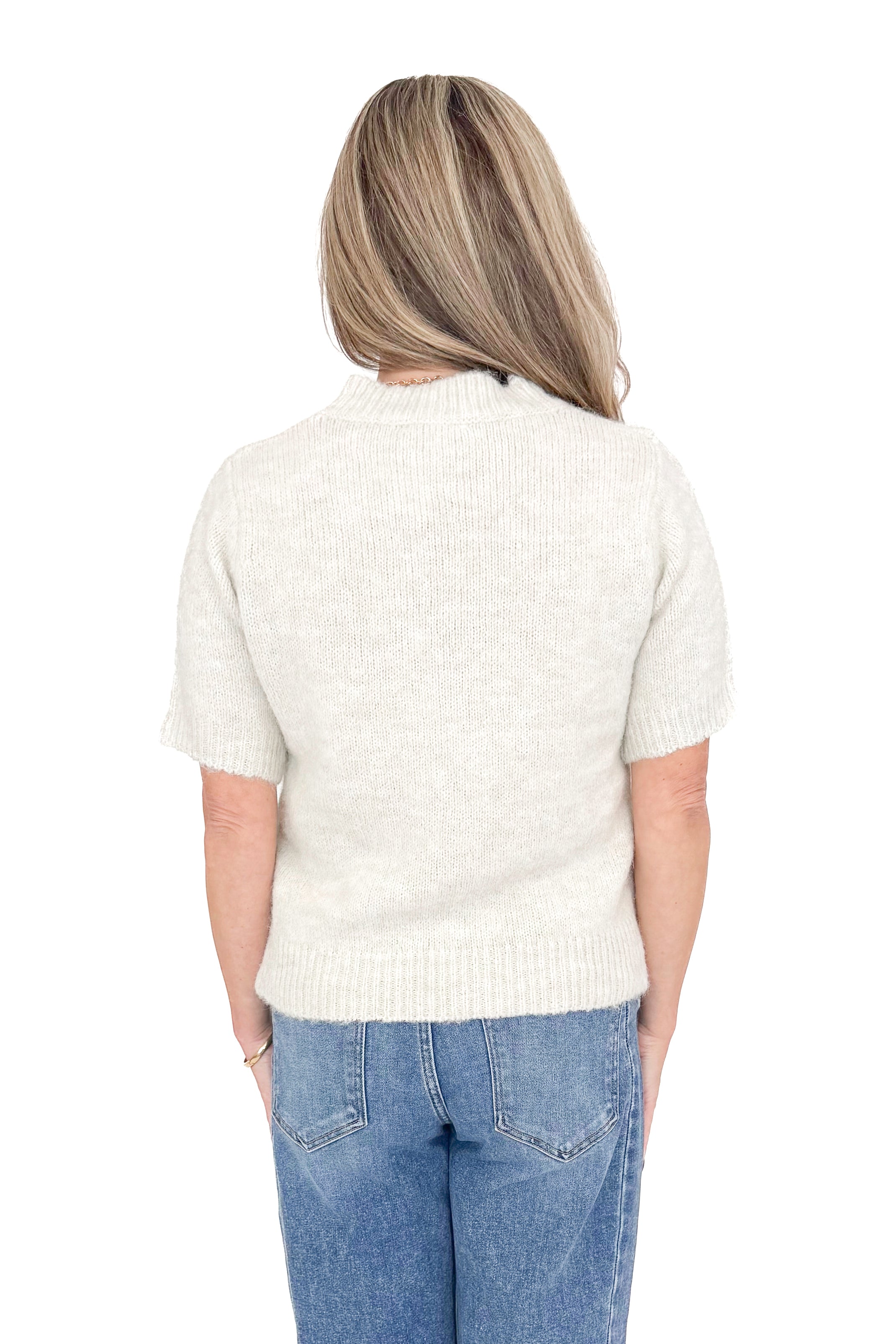 Back view of woman wearing oatmeal color sweater with jeans against white studio background.