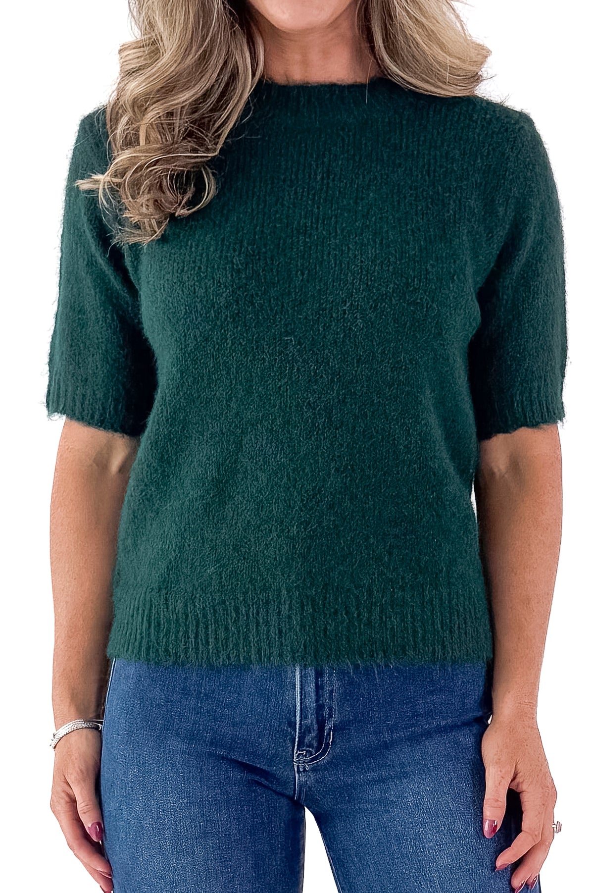 Front view of woman wearing green sweater with jeans and white studio background.