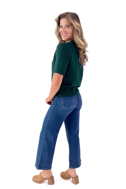 Side view of woman wearing green sweater with jeans and white studio background.