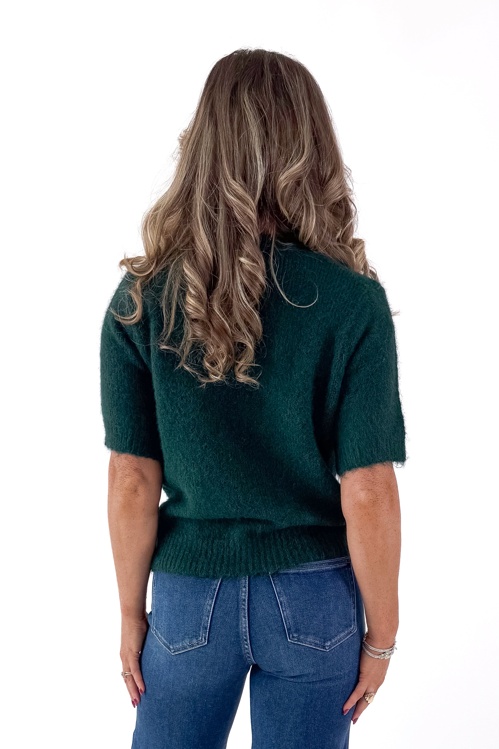 Back view of woman wearing green sweater with jeans and white studio background.