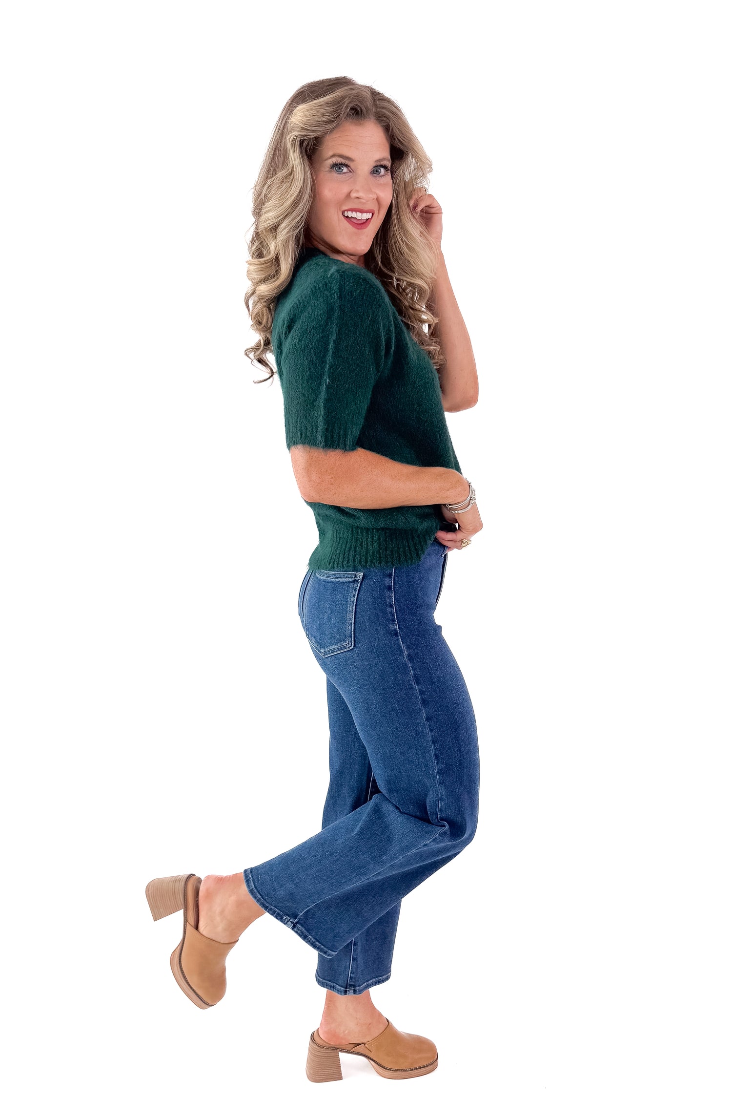 Side view of woman wearing green sweater with jeans and white studio background.