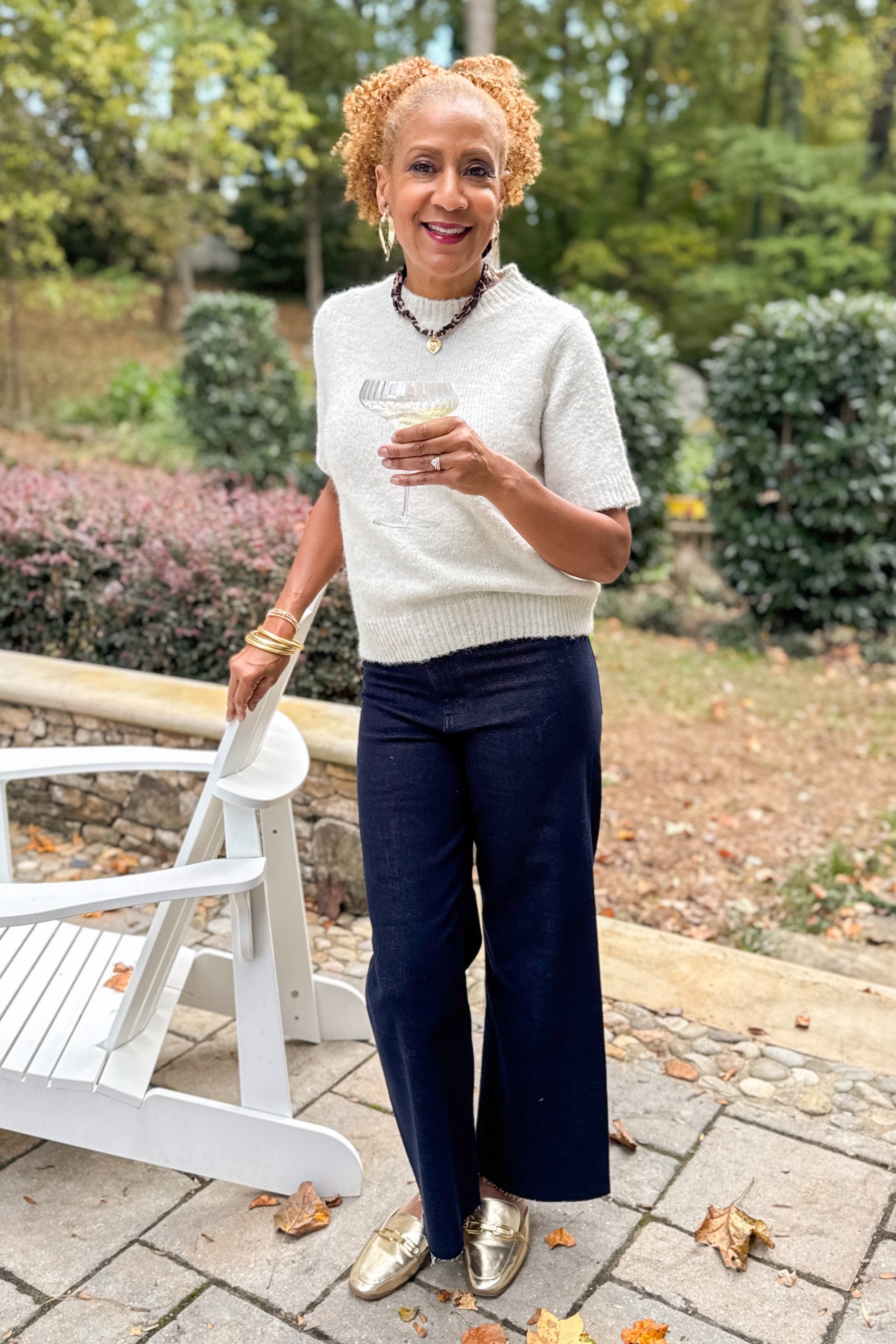 Front view of woman outside holding champagne wearing oatmeal color sweater with jeans.