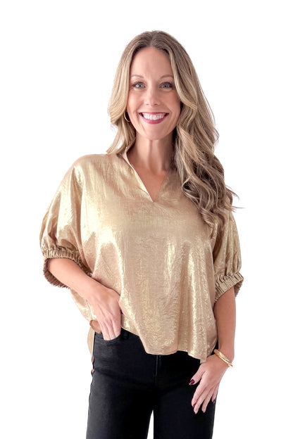Front view of woman wearing gold metallic top with black jeans against white studio background.