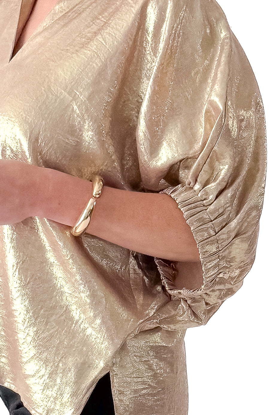 Side detail view of woman wearing gold metallic top with black jeans against white studio background.