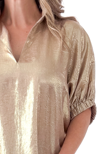 Front detail view of woman wearing gold metallic top with black jeans against white studio background.