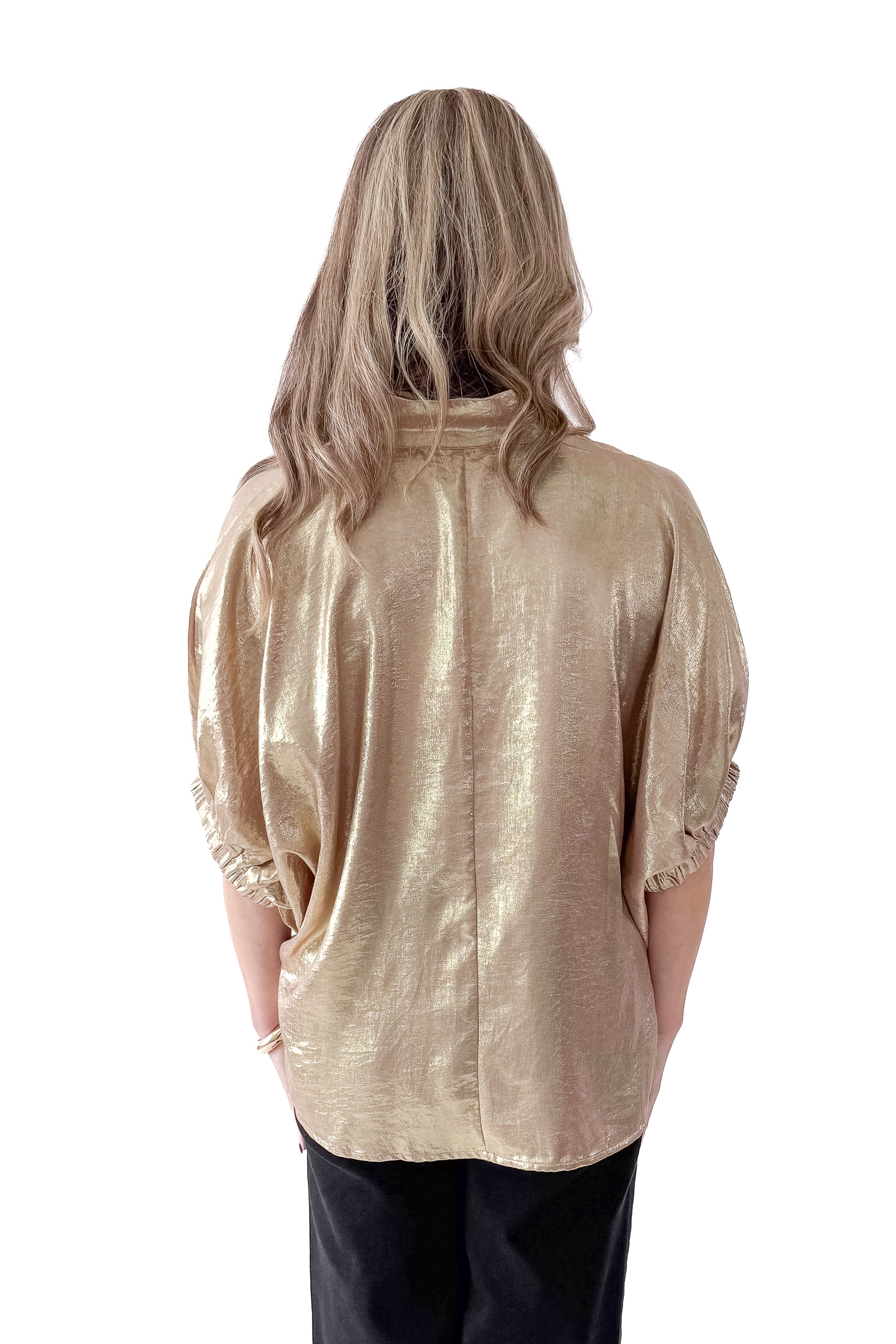Back view of woman wearing gold metallic top with black jeans against white studio background.