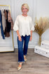 Woman wearing cream scallop hem sweater with jeans and decor in background.