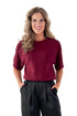Front view of woman wearing Burgundy Braid Detail Short Sleeve Sweater with black pants against white studio background.